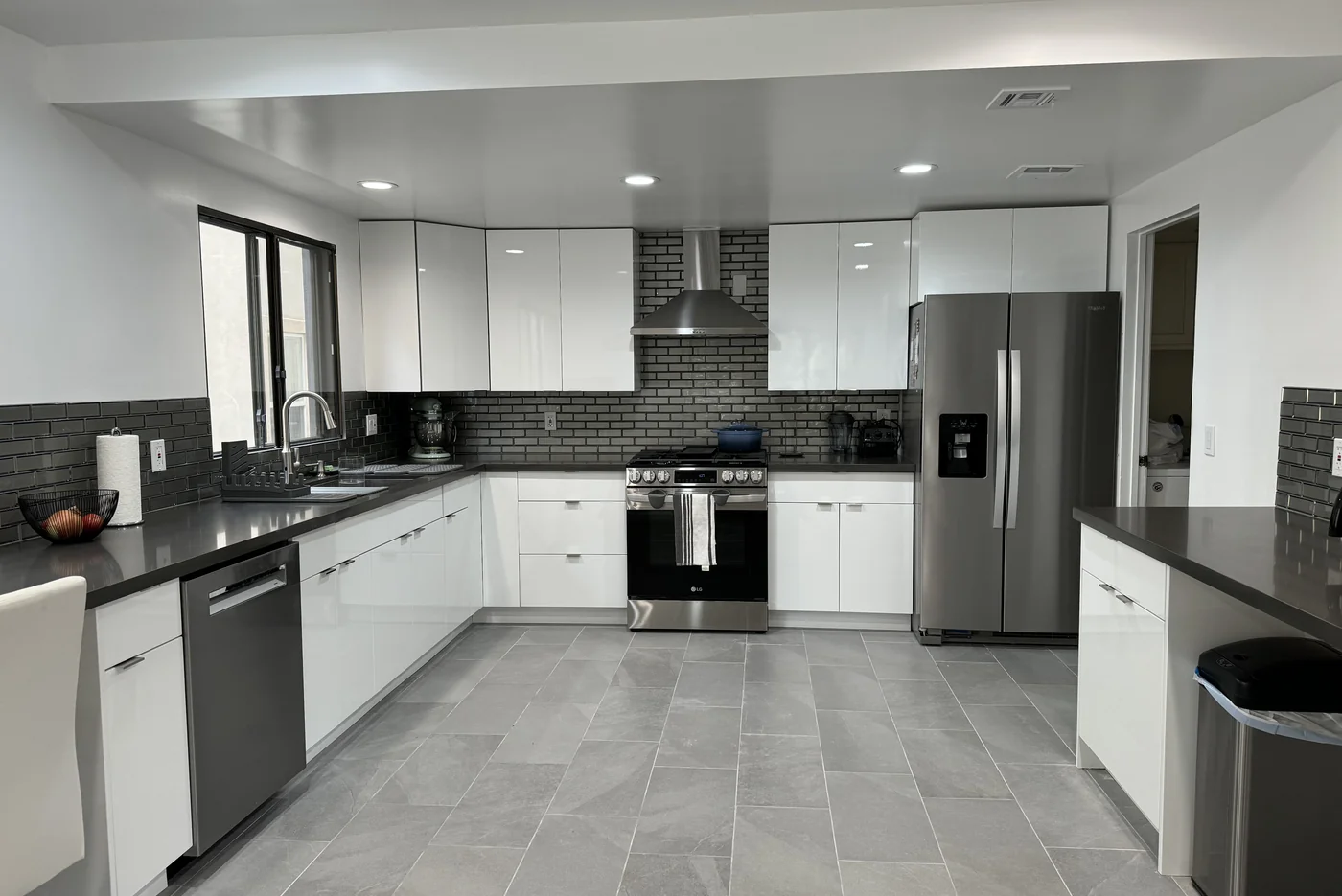 Glossy white kitchen in Burbank with cement-gray countertops, a gray glass backsplash, and stainless steel appliances
