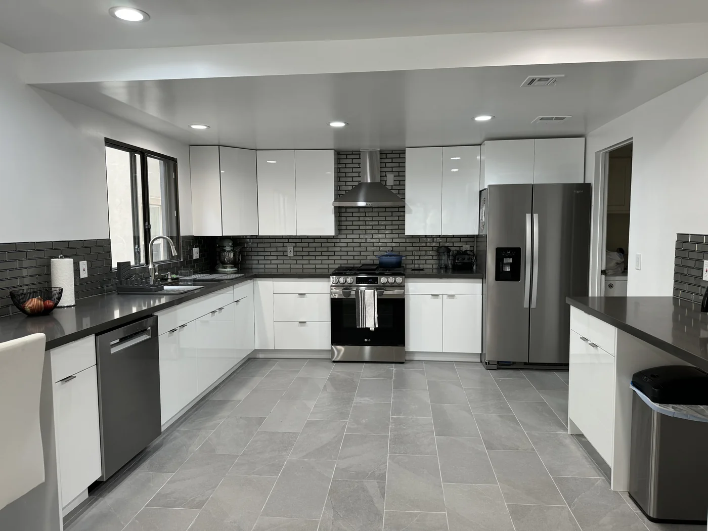 Glossy white kitchen in Burbank with cement-gray countertops, a gray glass backsplash, and stainless steel appliances
