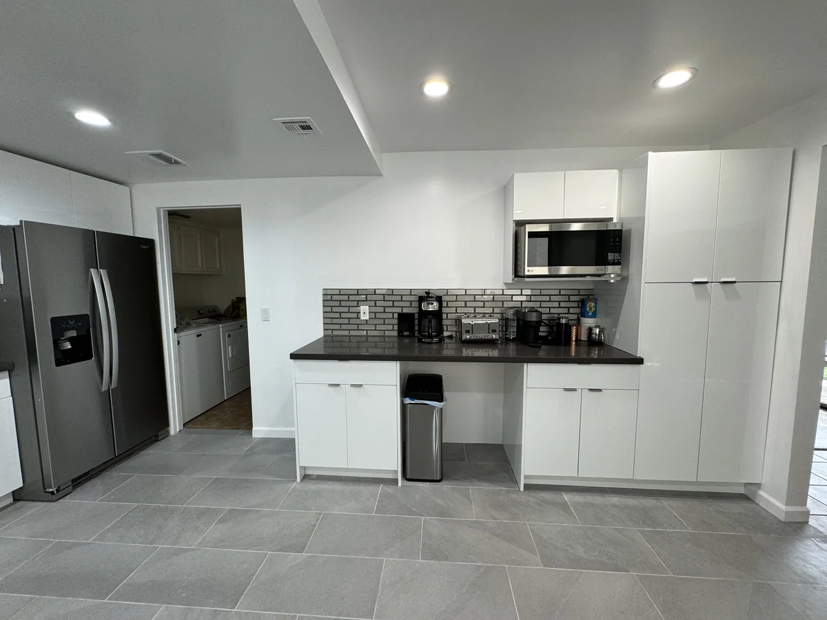 Built-in microwave and counter area beside glossy white storage cabinets and a stainless steel refrigerator