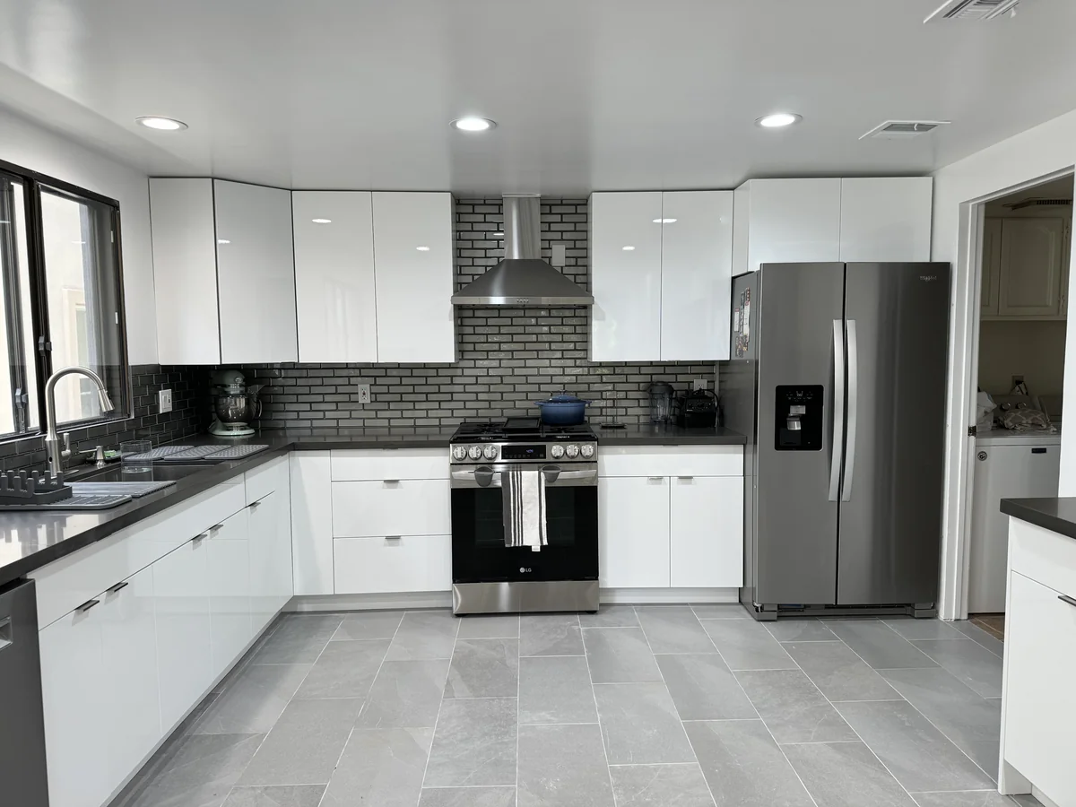 Stainless steel range and hood between white cabinets with cement-gray countertops and a gray glass backsplash