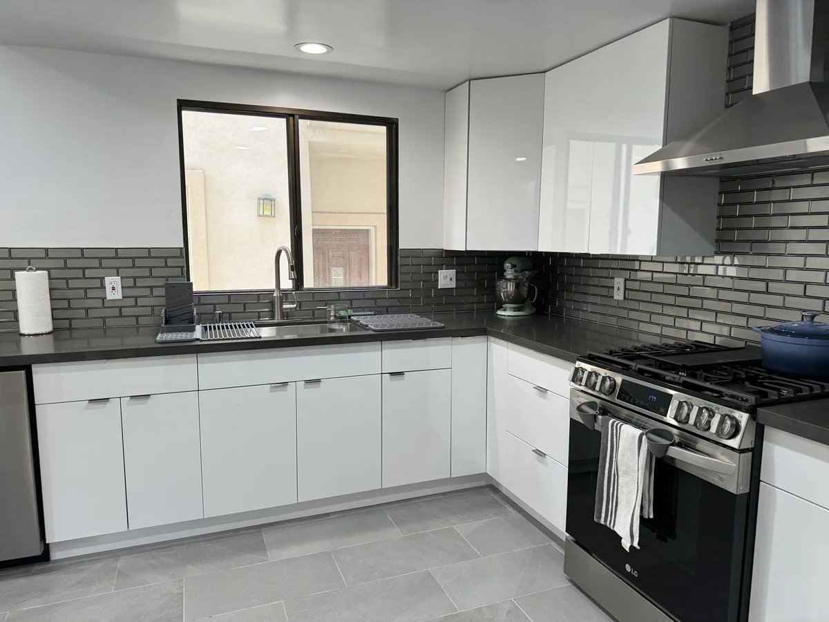 Corner kitchen cabinets and cement-gray work surfaces around the sink and stainless steel range