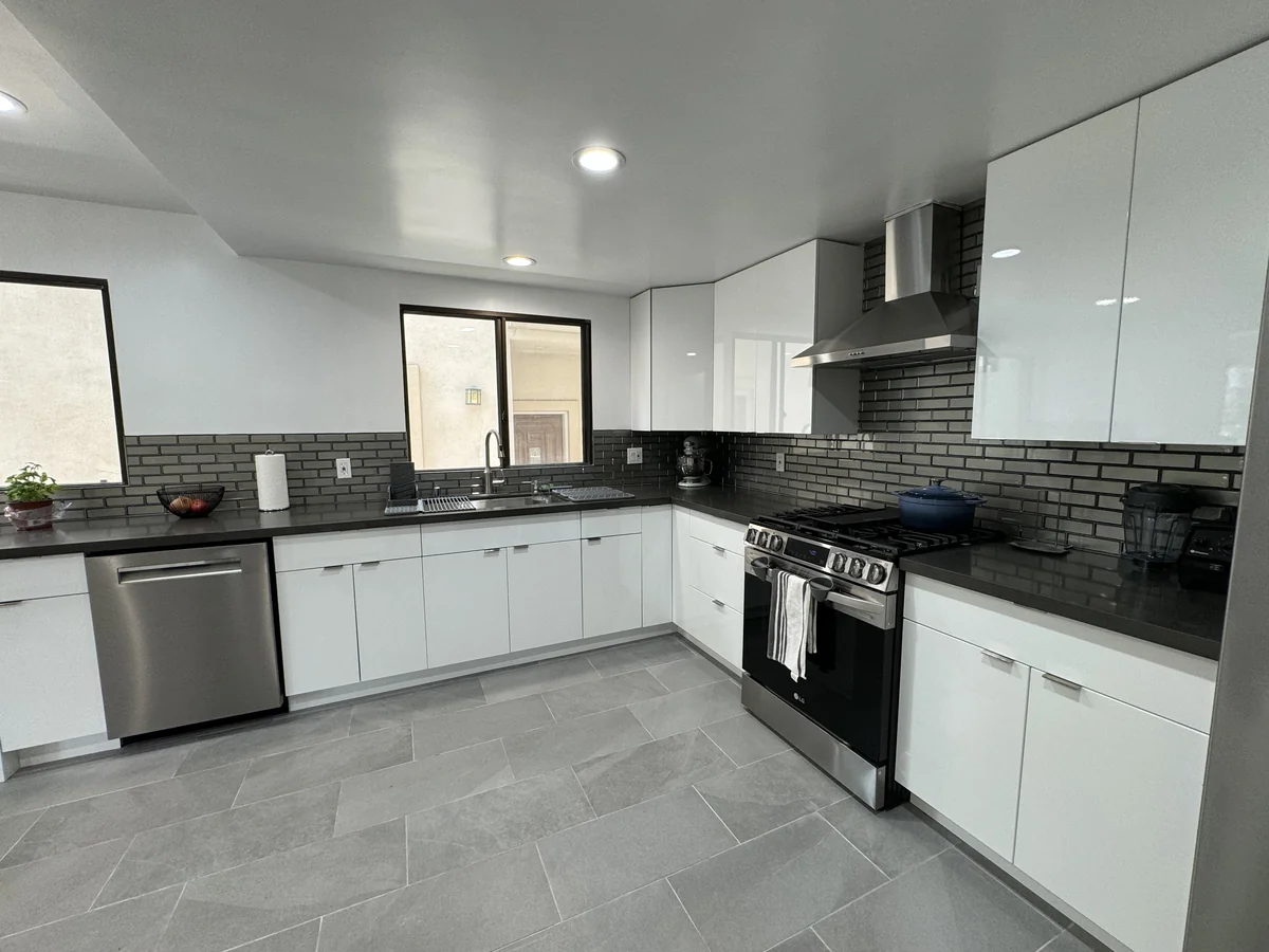 Glossy white upper and lower cabinets with a gray glass backsplash and recessed ceiling lights