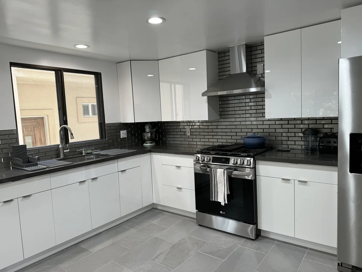 Stainless steel range and hood beside the window and glossy white corner cabinets