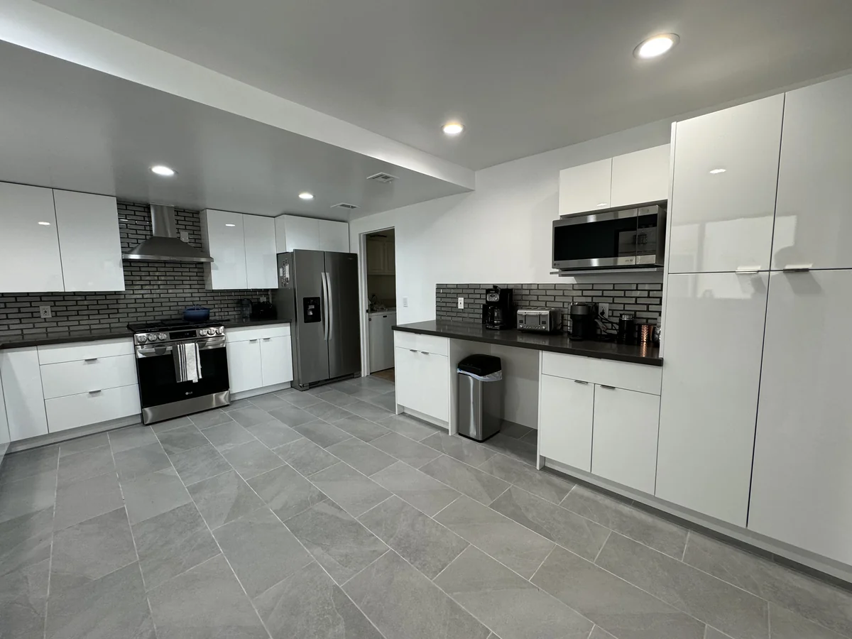 Wide view of white kitchen cabinetry, the refrigerator, and a separate microwave counter