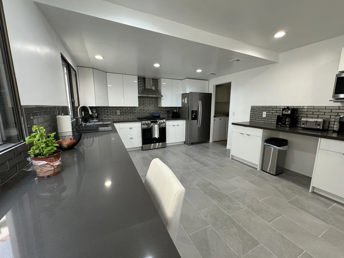 Breakfast counter beside a large window overlooking the white kitchen and gray tiled floor
