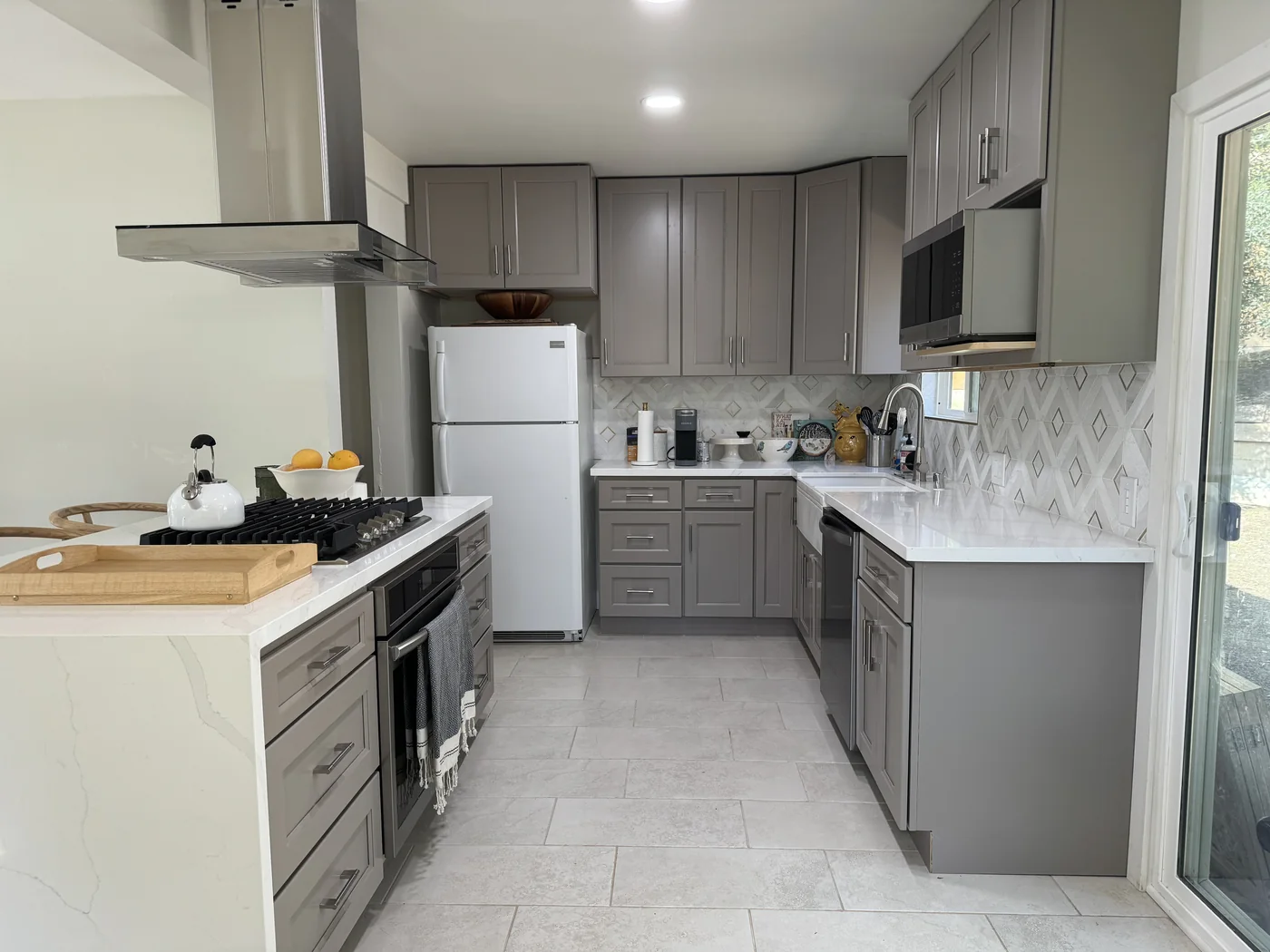 Gray shaker kitchen in Sunland with light countertops, a patterned backsplash, and a stainless steel hood