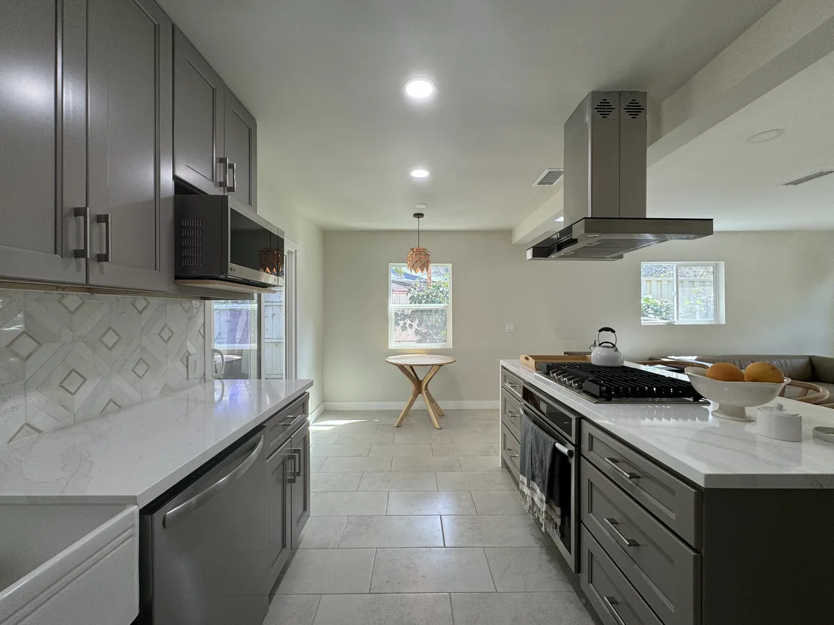 Gray kitchen cabinets and light countertops leading toward a round dining table beside the window