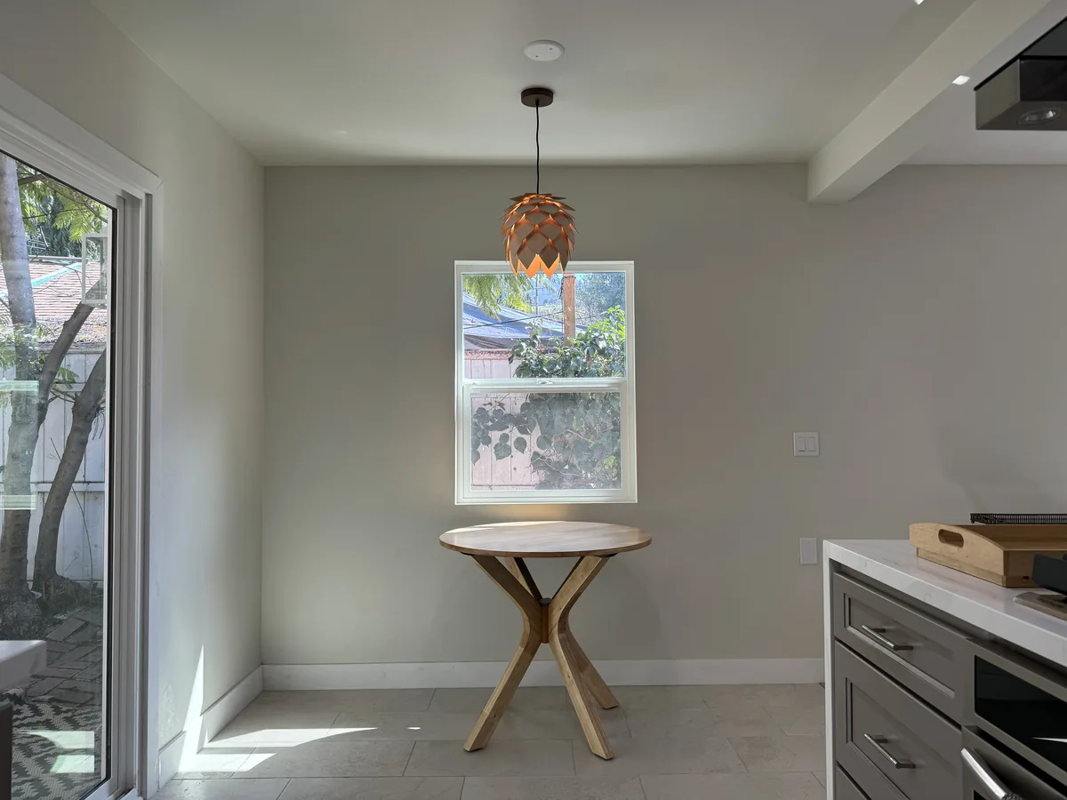 Round wooden dining table beneath a pendant light beside the kitchen and sliding glass doors