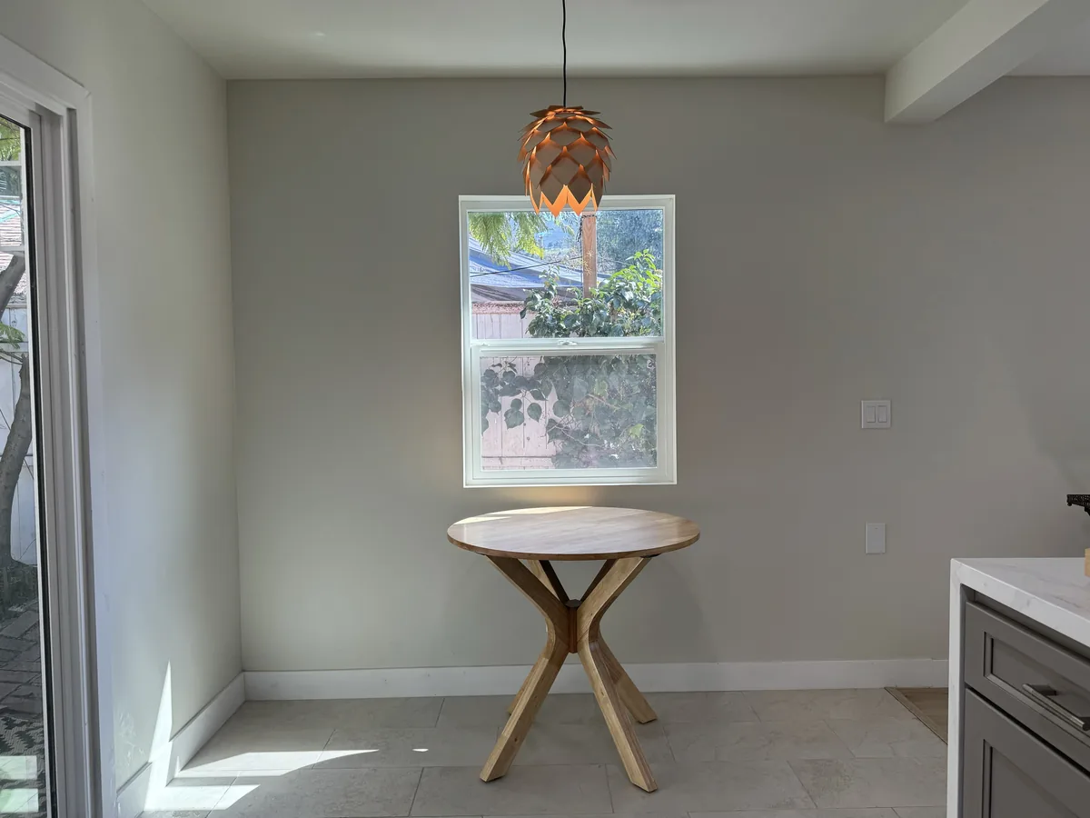 Sunlit dining nook with a round wooden table, a window, and a sculptural pendant light