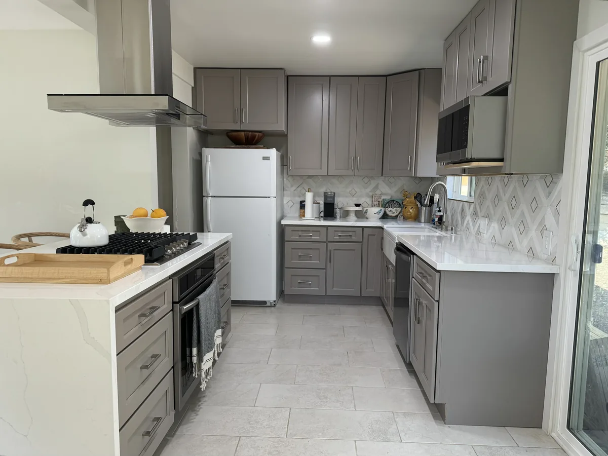 Gray shaker cabinets surrounding a refrigerator with a light patterned backsplash and peninsula range
