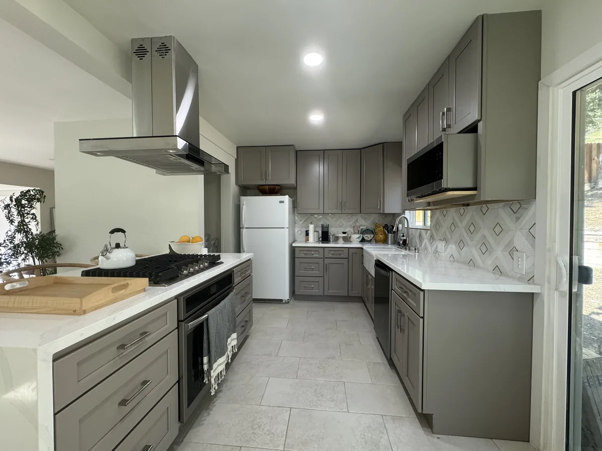 Kitchen aisle between gray cabinets with the range in the peninsula and a stainless steel hood above