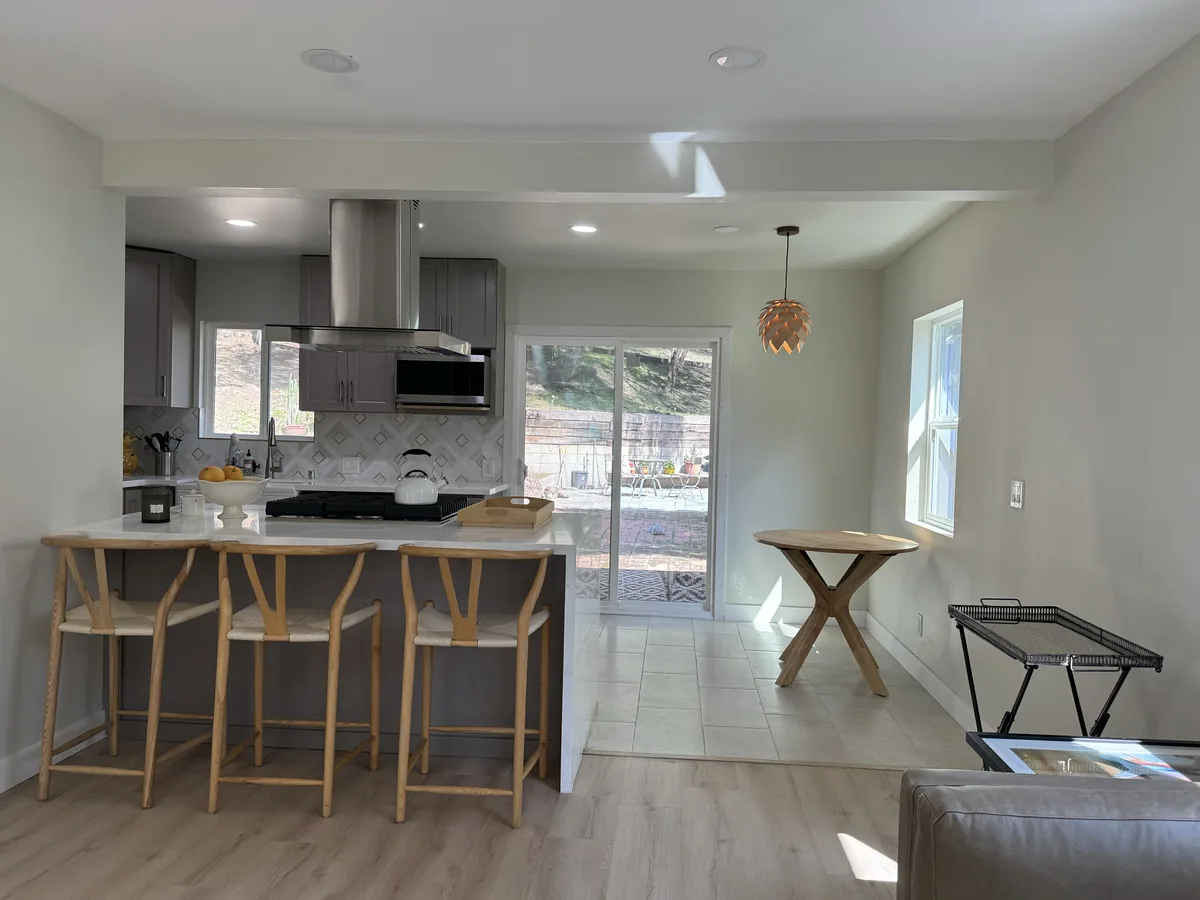 Wide view of the gray kitchen breakfast bar, wood stools, dining nook, and glass doors