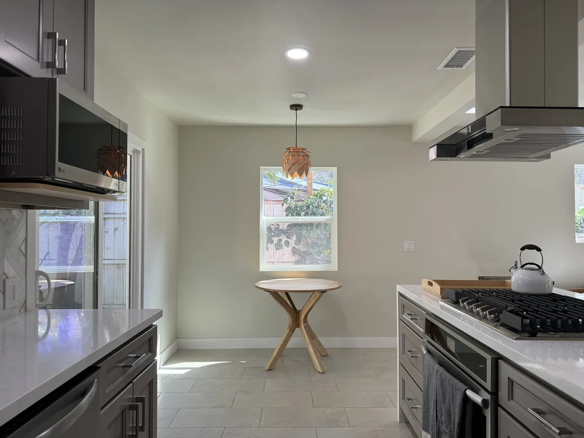 View between gray kitchen cabinets toward the dining nook with a pendant light and round wooden table