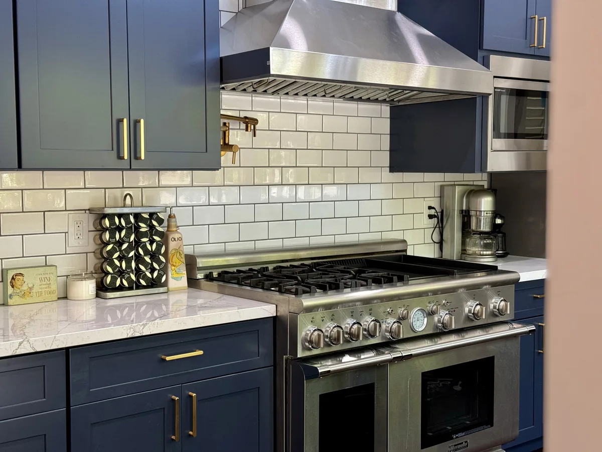 Stainless steel range and hood framed by blue cabinets and white tile backsplash