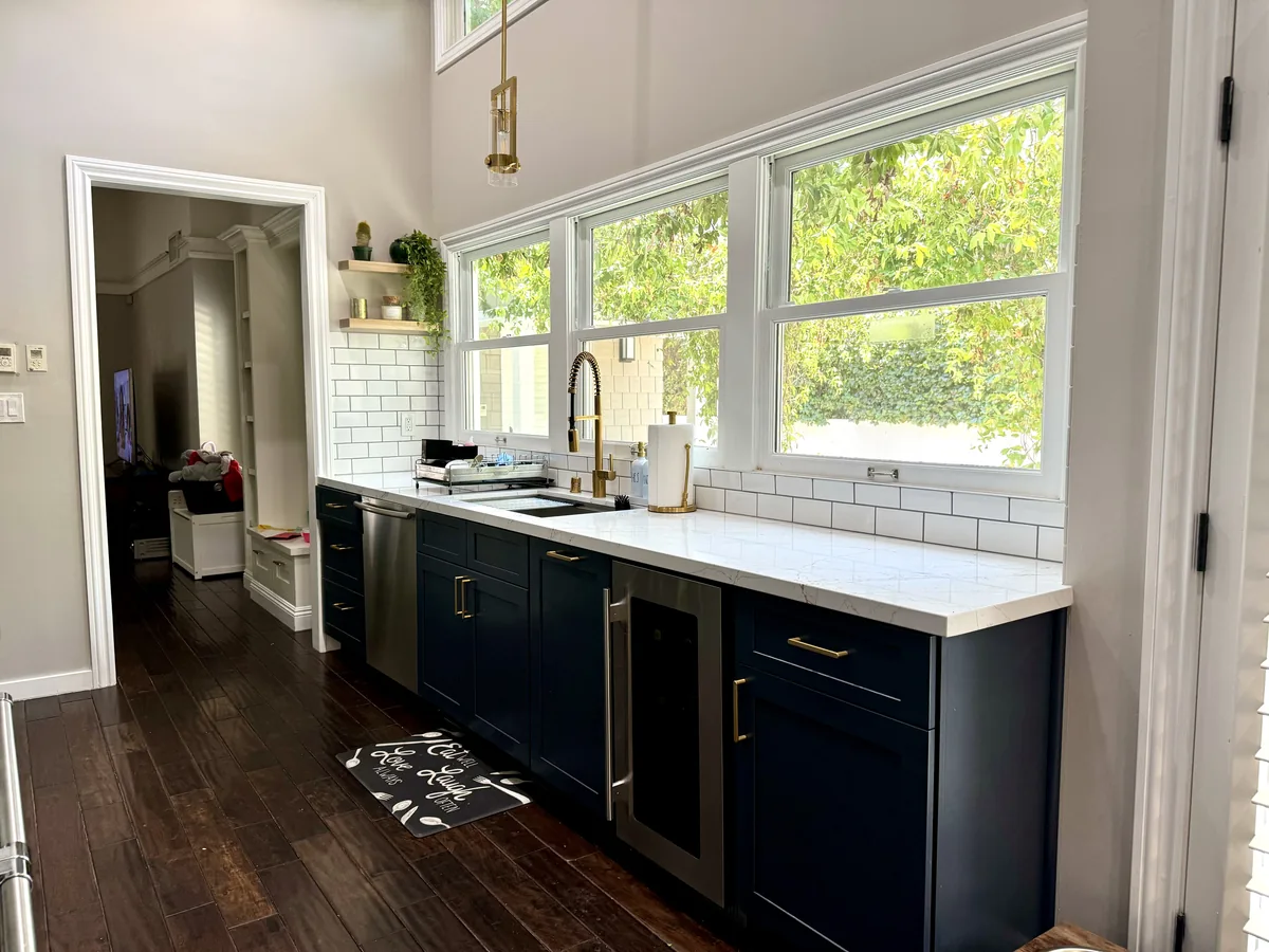 Kitchen sink below large windows with blue lower cabinets and white quartz countertops