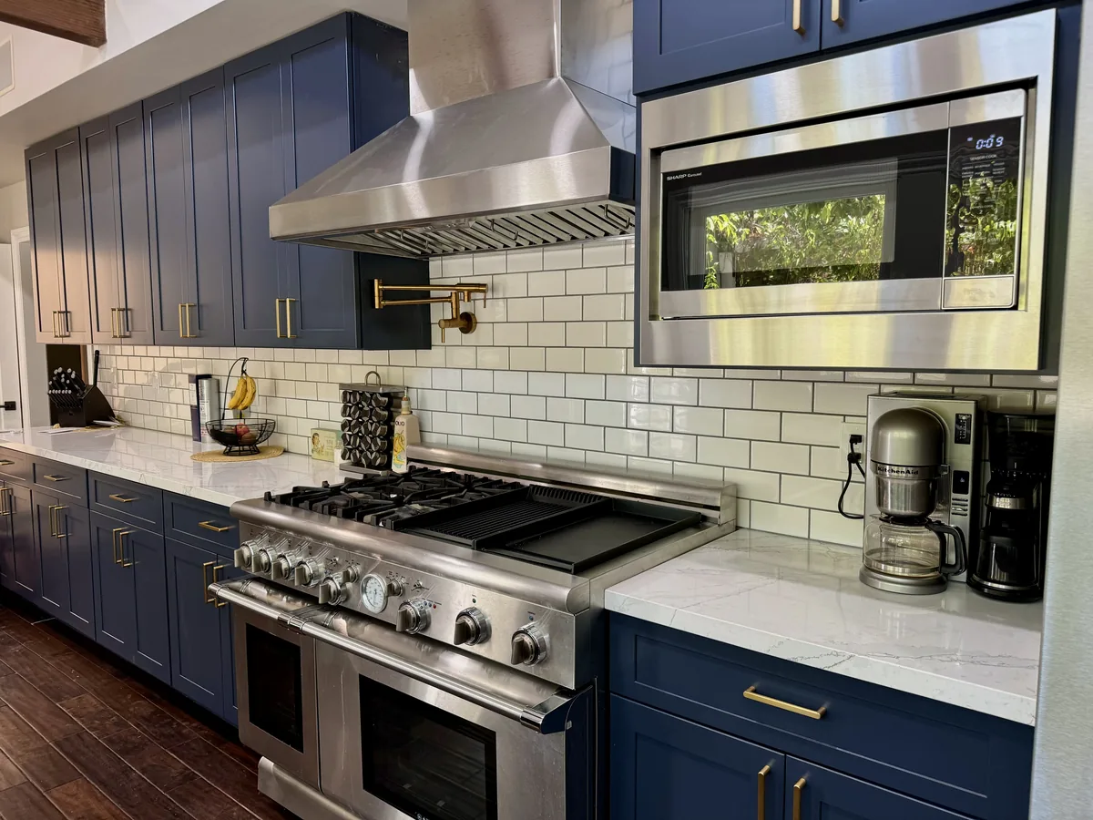 Blue kitchen cabinets surrounding a stainless steel range, hood, and built-in microwave