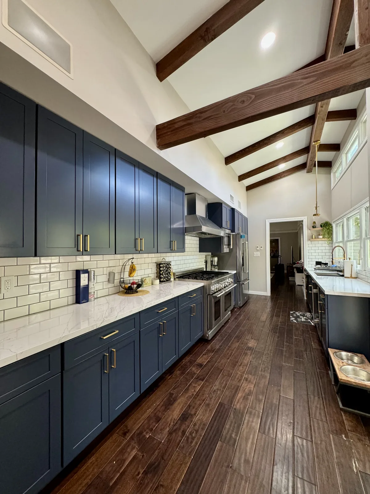 Full view along the blue cabinets beneath the vaulted ceiling and wood beams