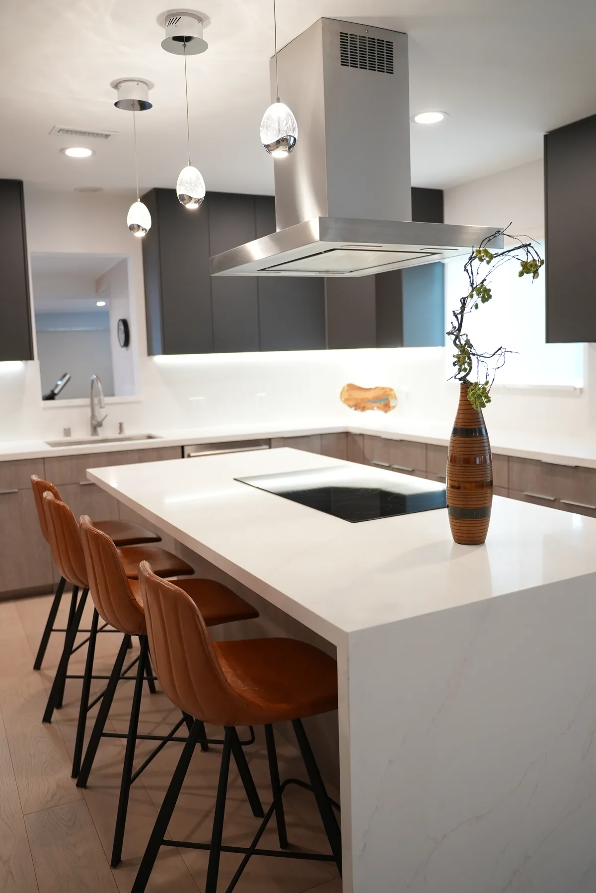 Island cooktop, stainless steel hood, and a row of brown bar stools