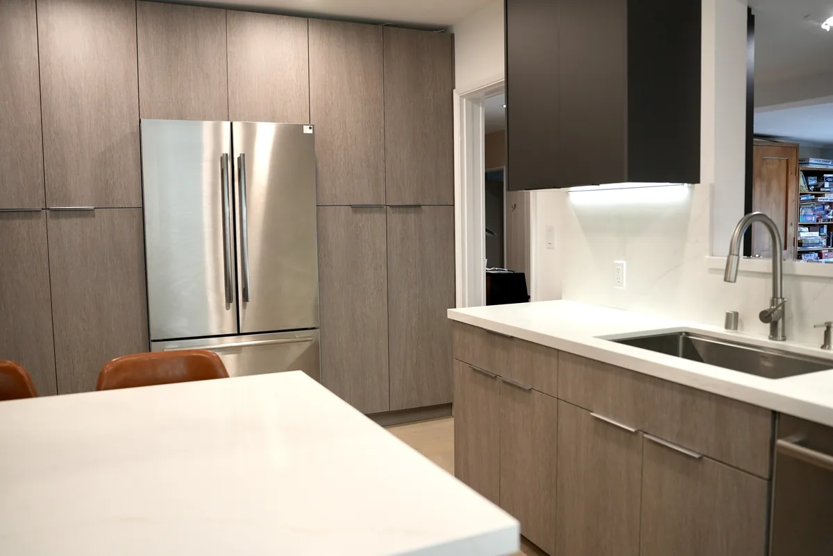 Refrigerator surrounded by wood-tone cabinetry across from the white island