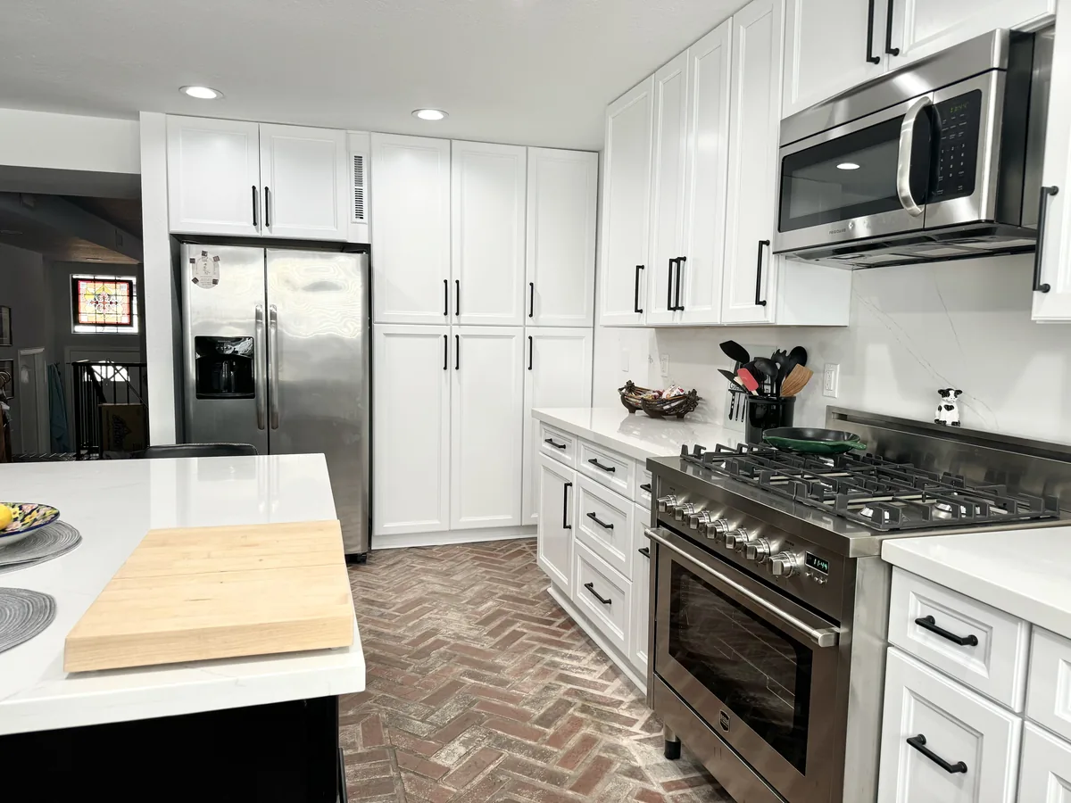 View past the kitchen island toward the range, refrigerator, and tall white pantry cabinets
