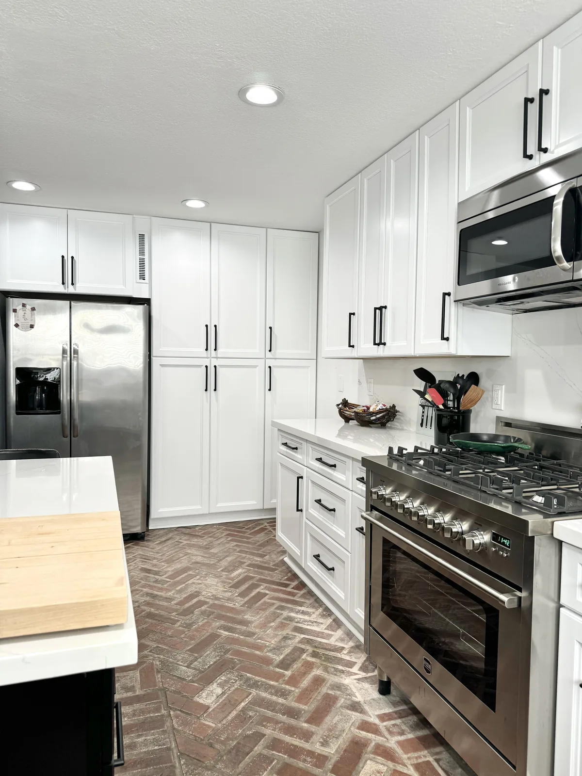 Stainless steel refrigerator and range surrounded by white shaker cabinetry
