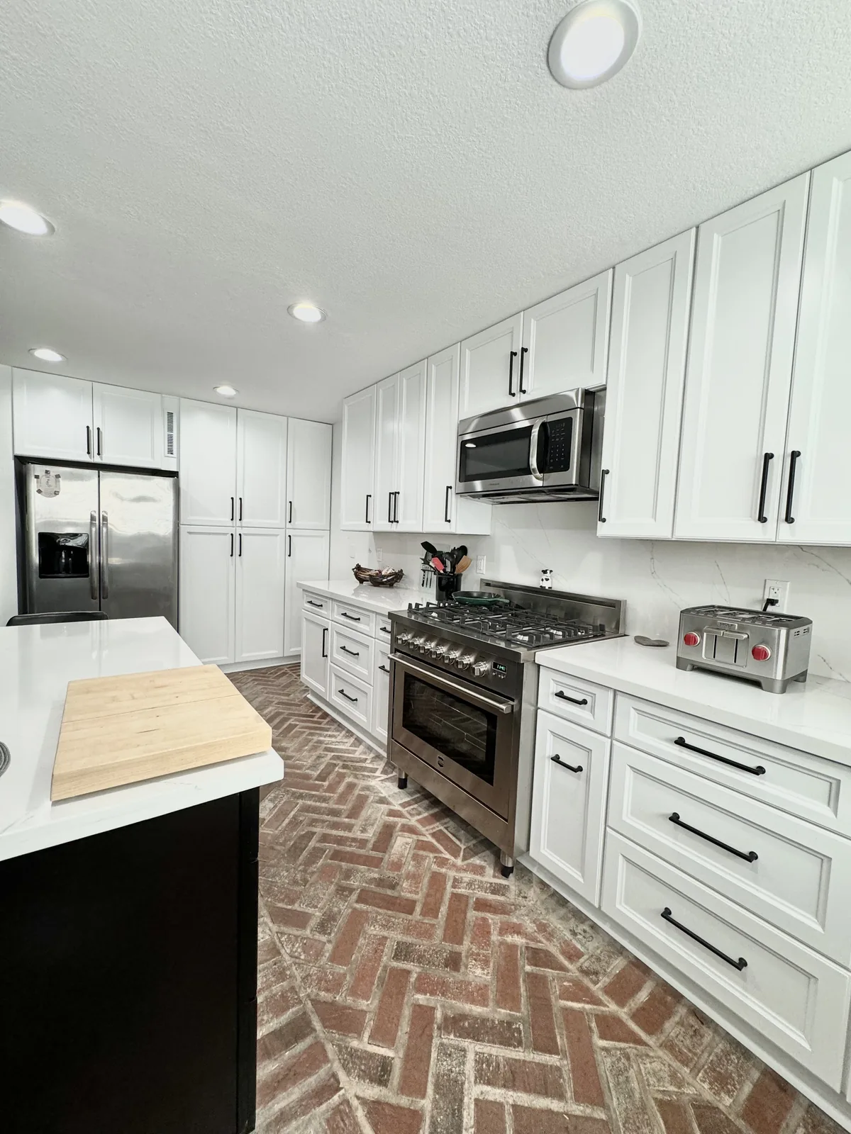 Long view of white kitchen cabinetry alongside the island and patterned floor