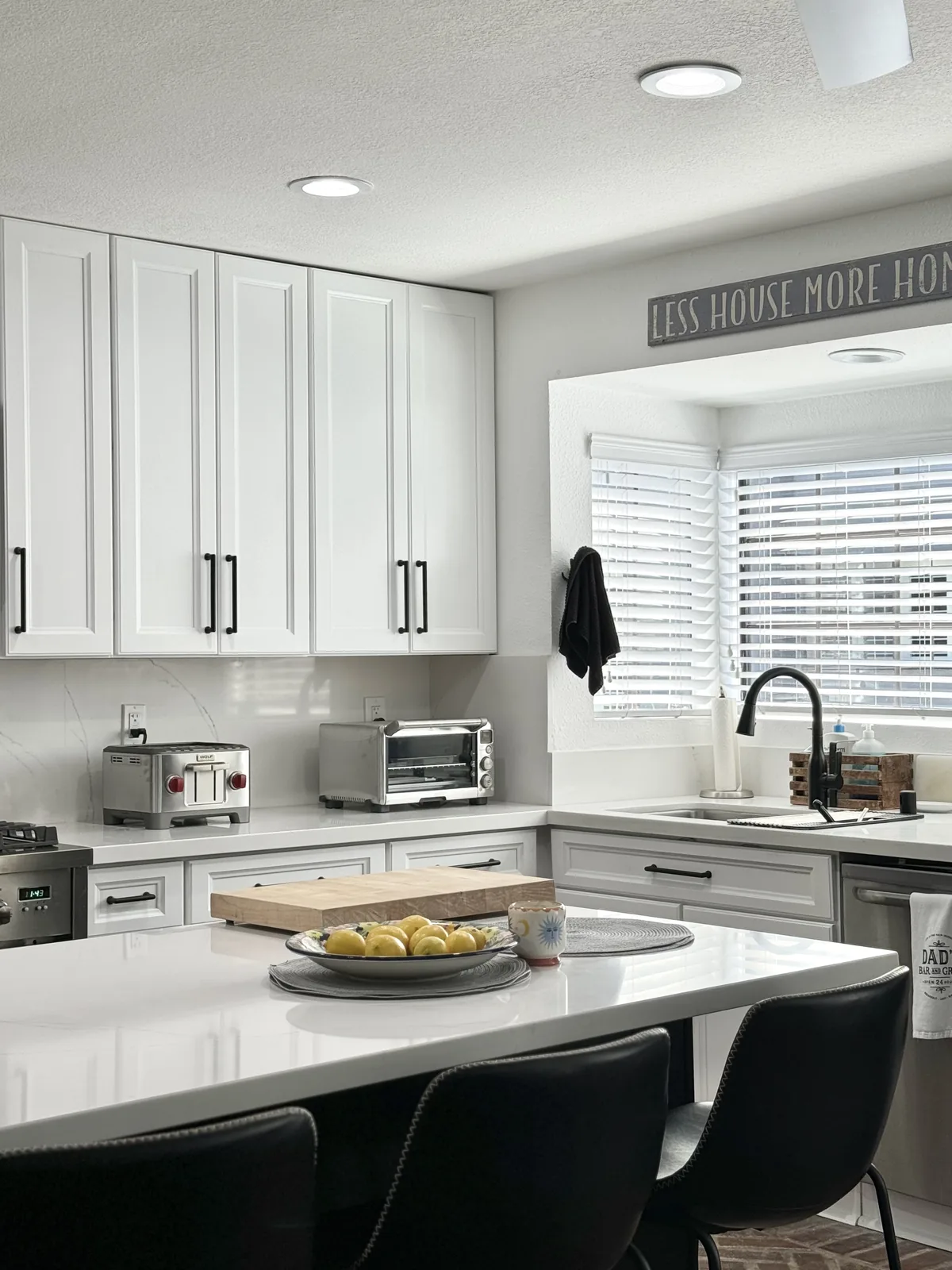 Island seating in front of white cabinets and the kitchen sink window