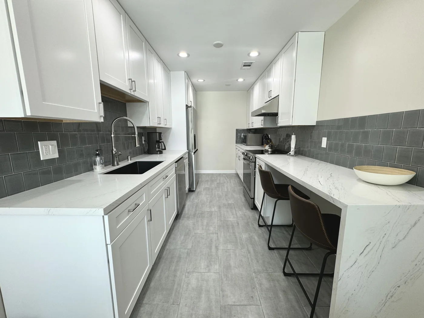 White shaker galley kitchen in Glendale with Calacatta quartz countertops, dark tile backsplash, and bar seating