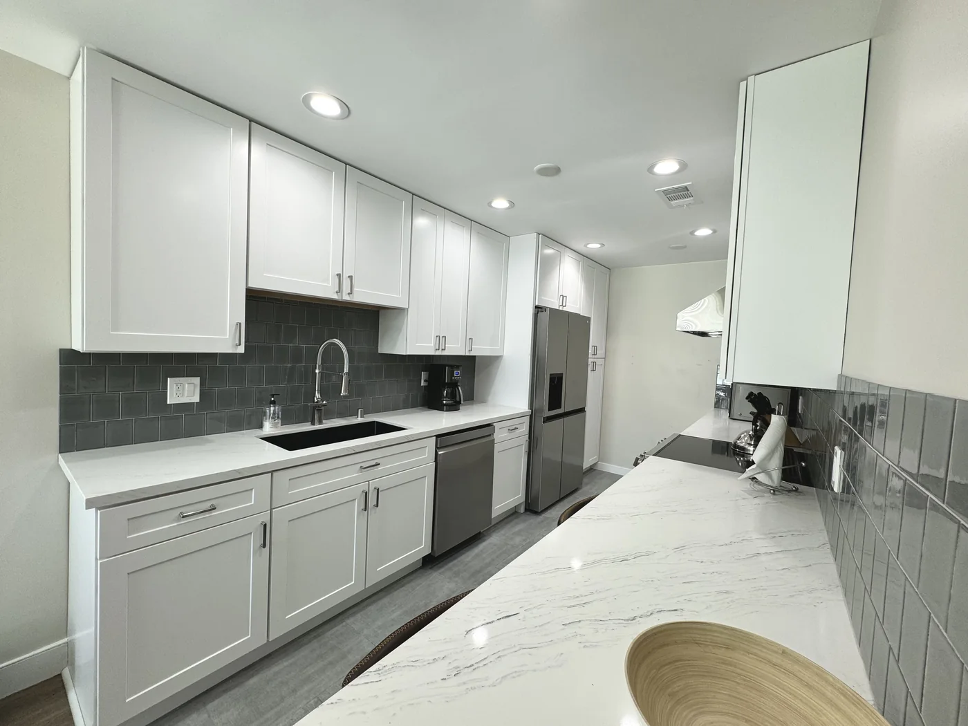 Wide view of white shaker cabinets and the sink counter opposite the quartz breakfast bar