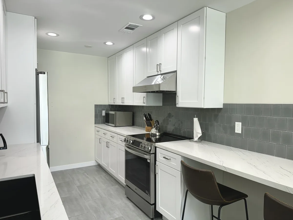 White upper cabinets above a stainless steel range and hood beside a quartz breakfast bar
