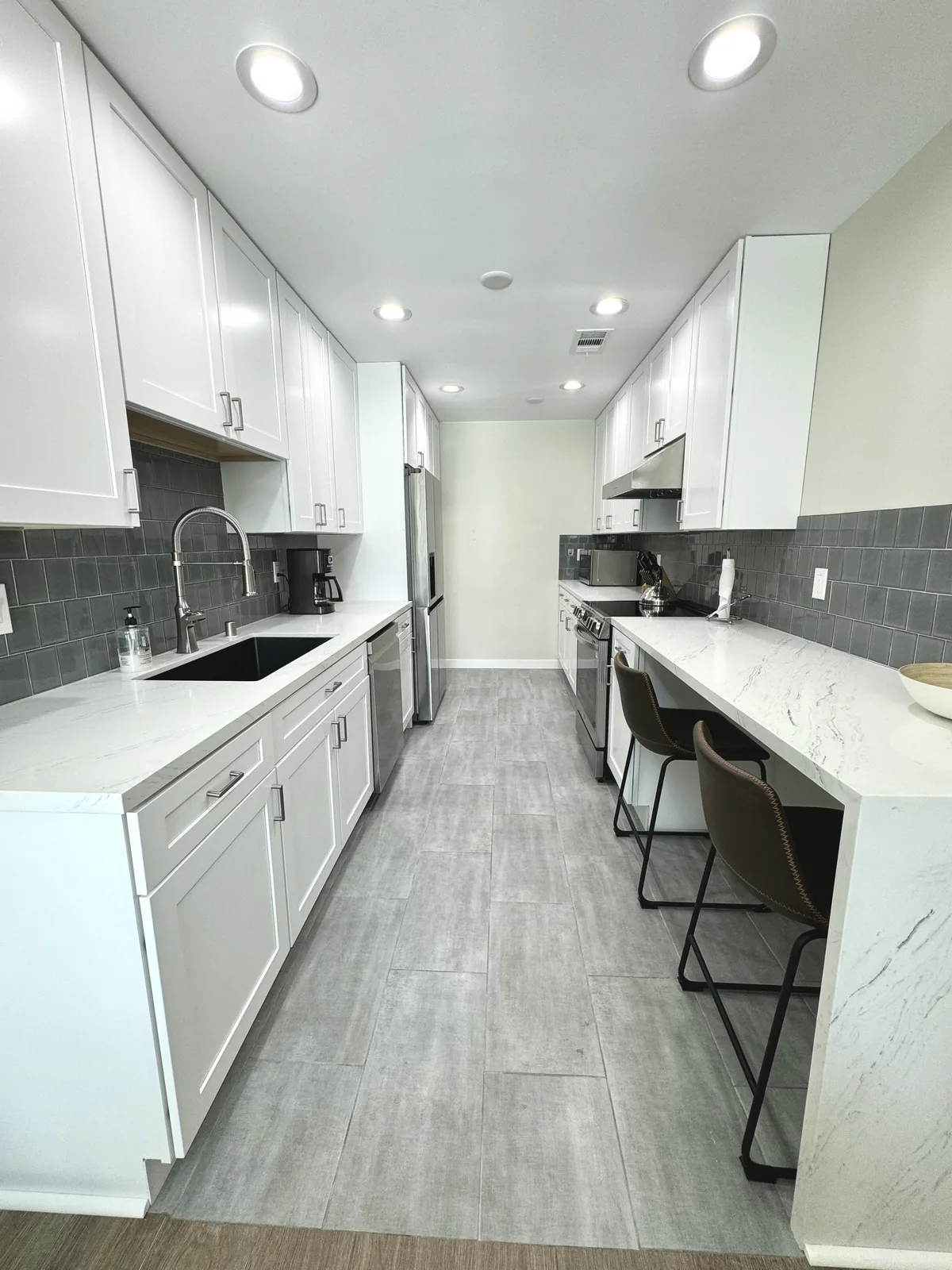 Full-length view of the white shaker galley kitchen with dark backsplash and gray flooring
