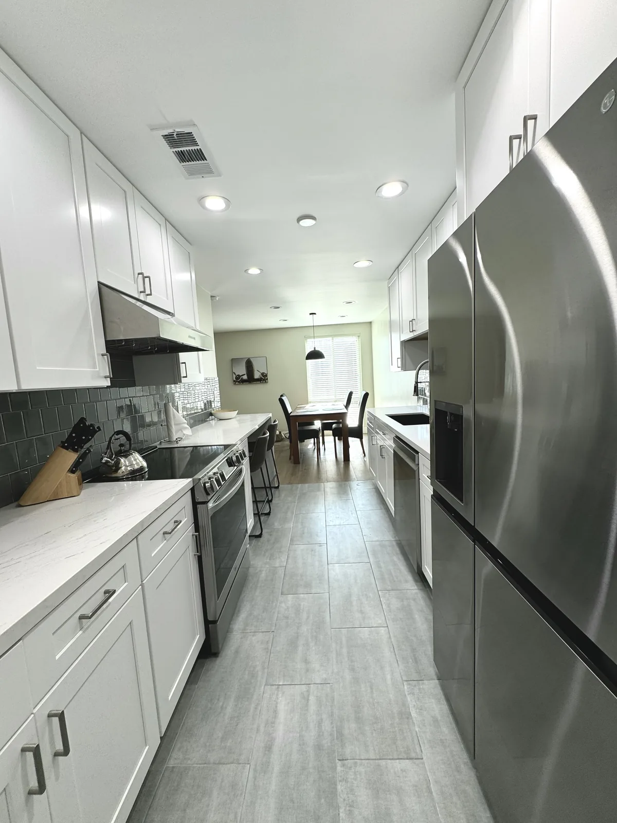 View toward the dining area between white kitchen cabinets and a stainless steel refrigerator