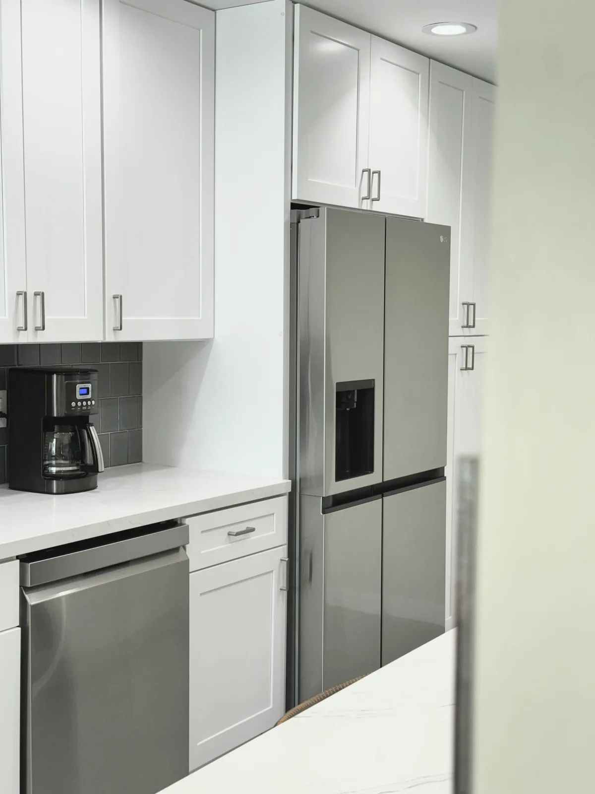 Stainless steel refrigerator and dishwasher beside white shaker cabinetry