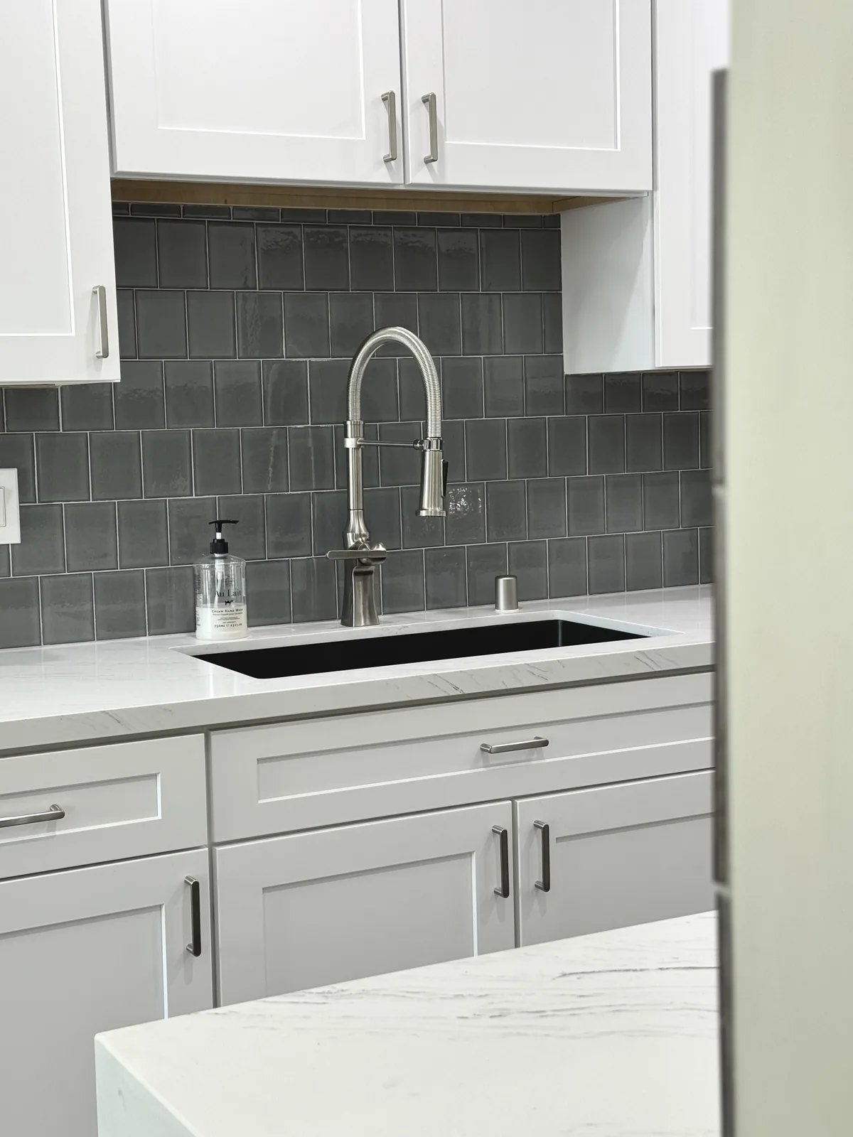Kitchen sink and tall curved faucet against a dark tile backsplash