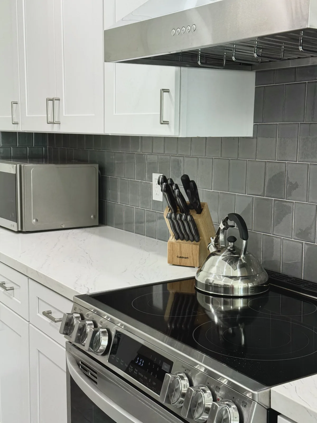 Stainless steel range with a kettle beneath a hood and white shaker cabinets