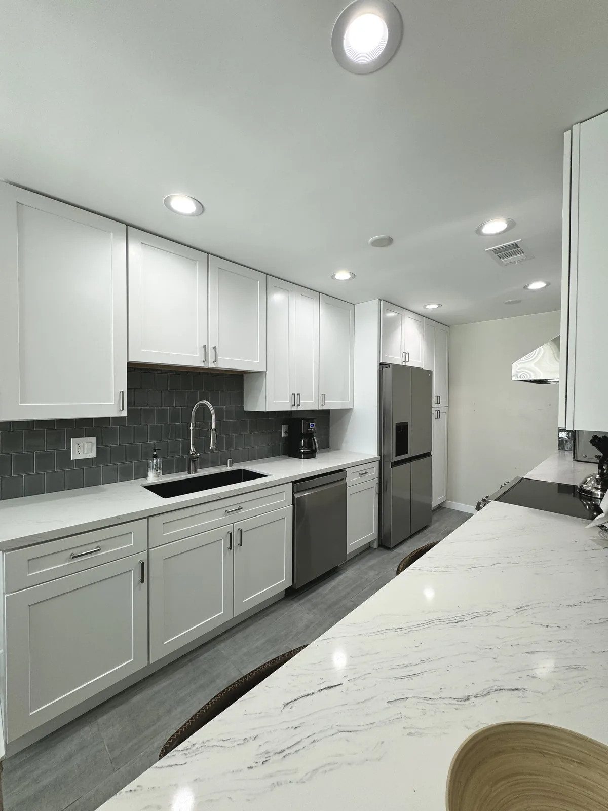 Long sink counter with white drawers and cabinets opposite the veined quartz breakfast bar