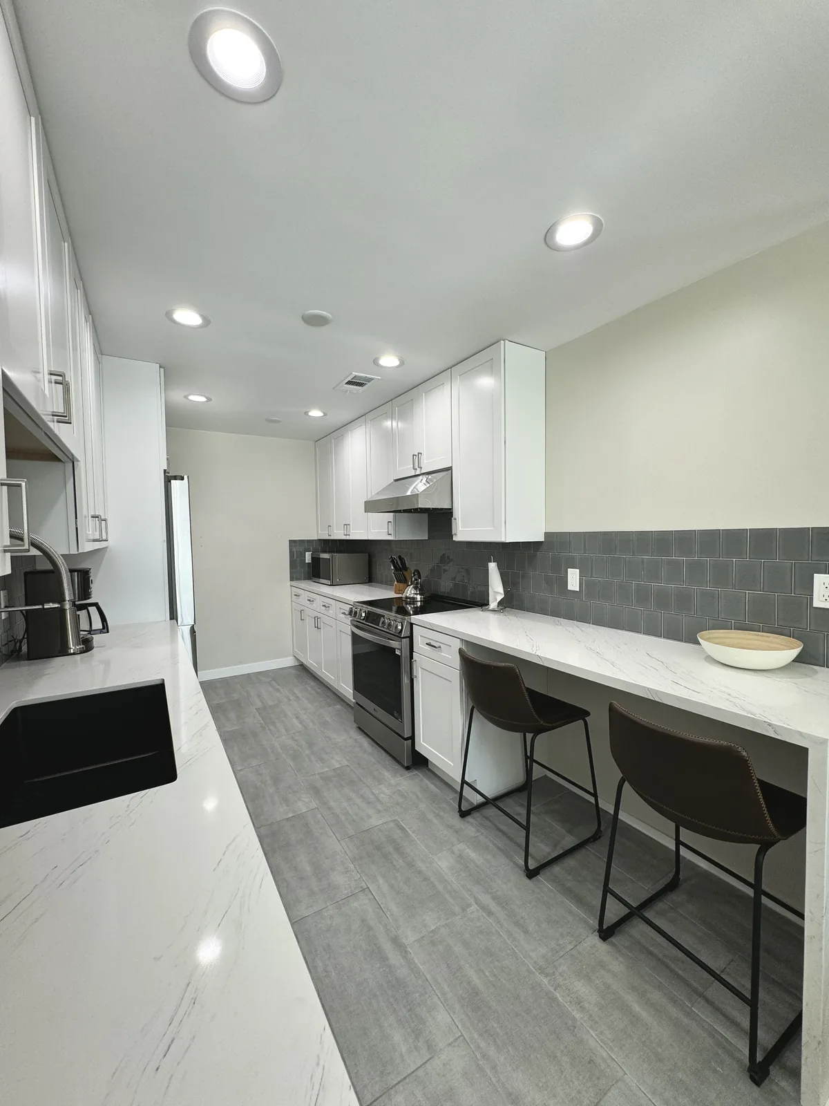 View down the Glendale kitchen toward the range, hood, and quartz bar with seating
